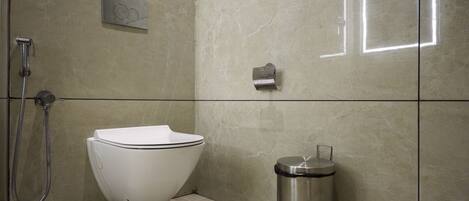 A modern bathroom with a toilet, a shower, and a trash bin.