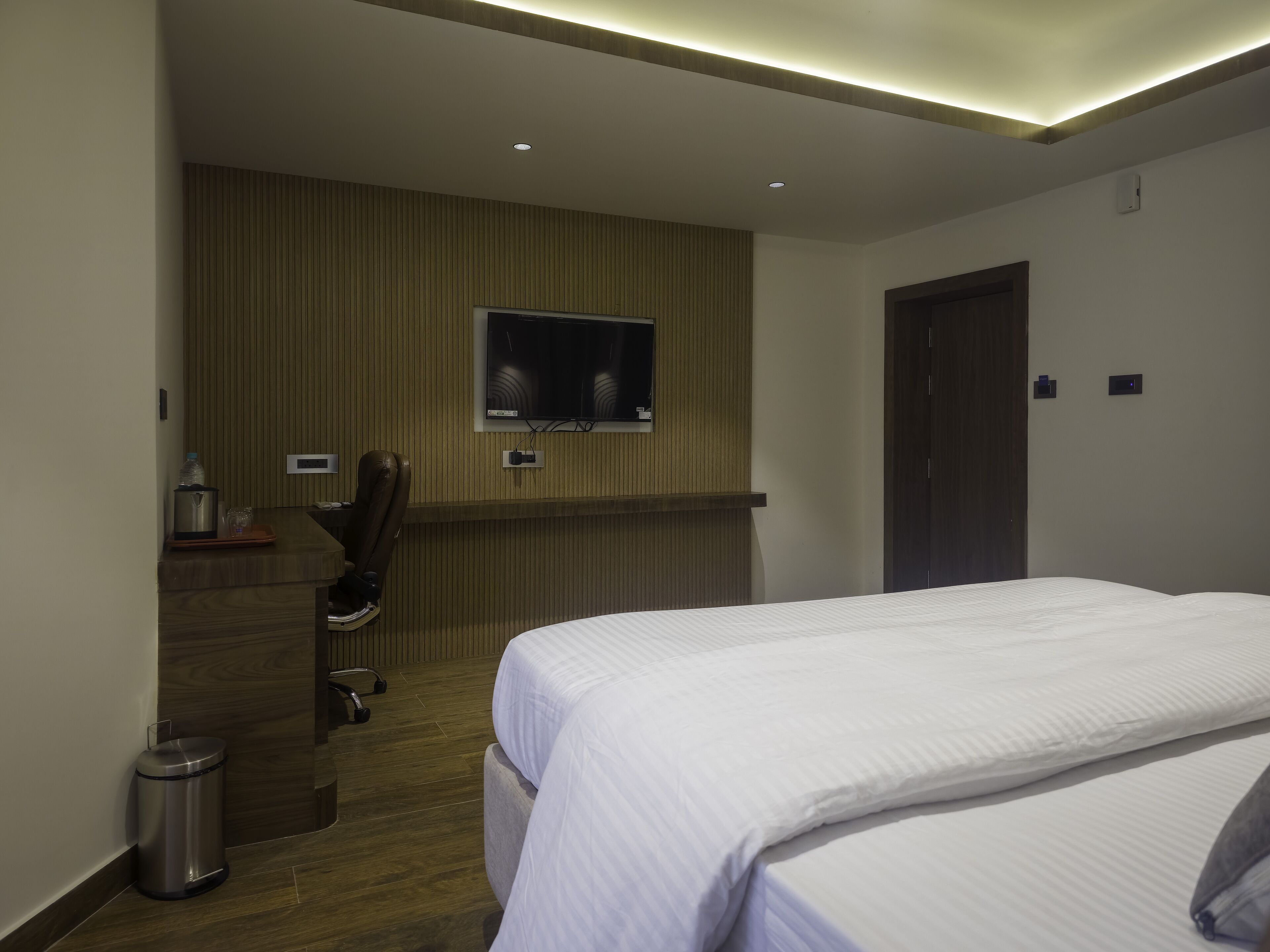Habitació d'hotel moderna amb un llit, un televisor fixat a la paret, una taula de treball amb una cadira i un paperer.
