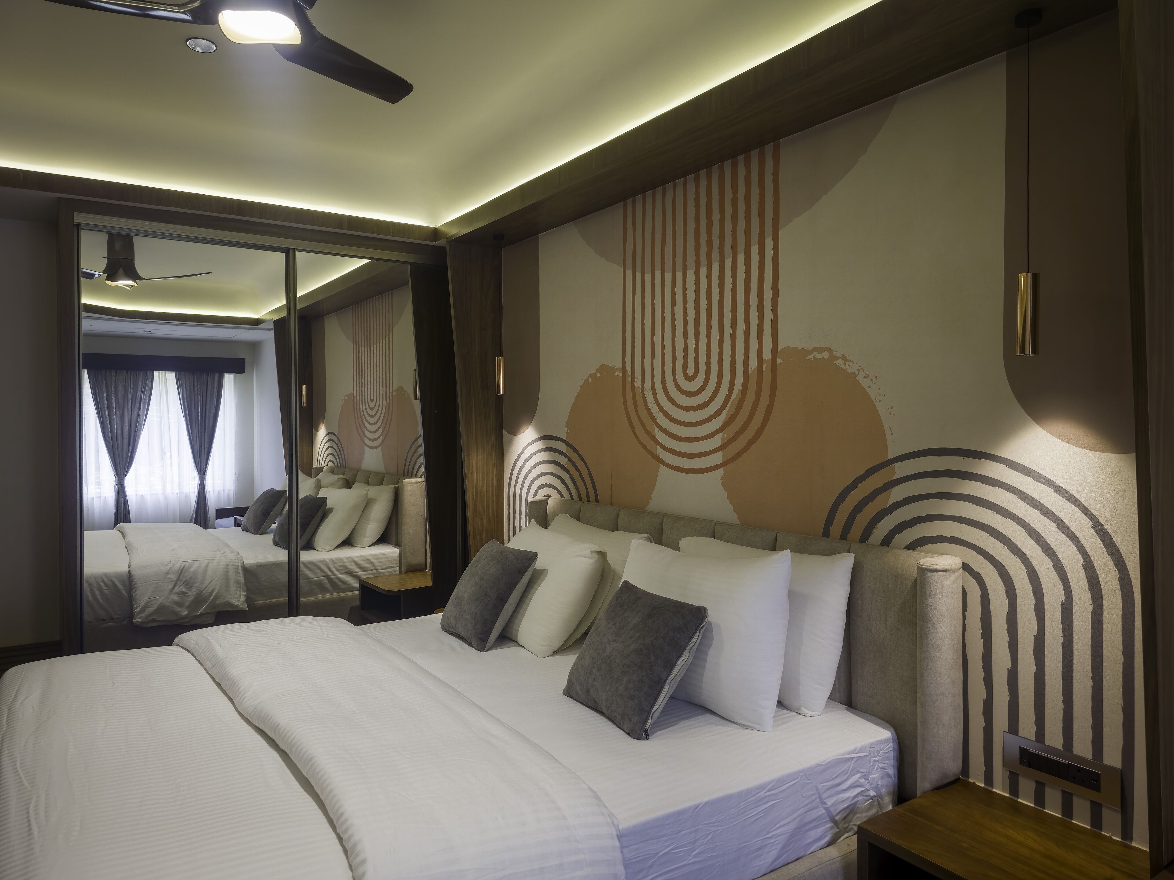 Una habitación de hotel moderna con una cama grande, una mesita de noche, un espejo y un ventilador de techo.