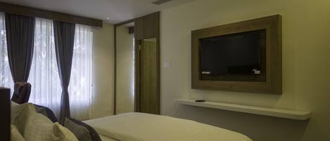 A hotel room with a bed, a ceiling fan, a mounted TV, and a window with curtains.
