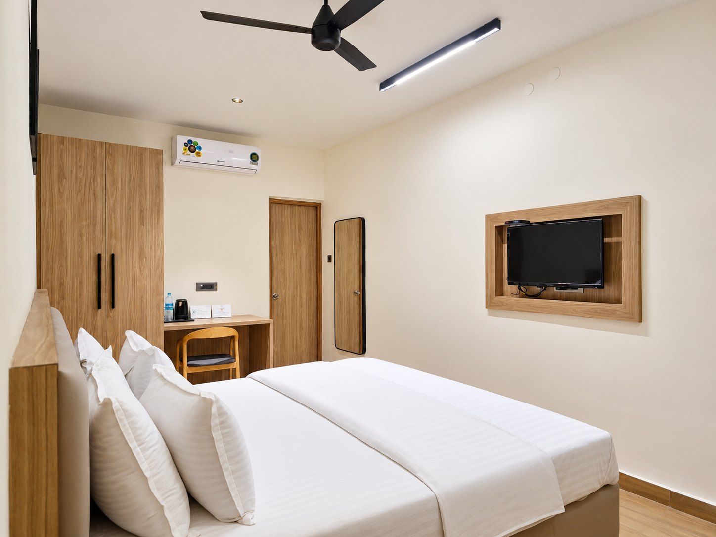 A hotel room with a bed, a desk, a television mounted on the wall, and a ceiling fan.