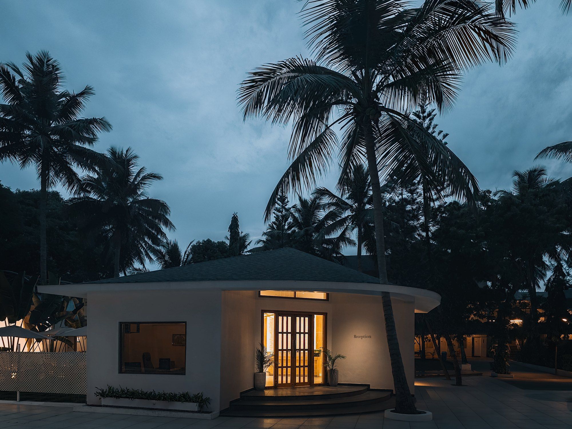 A small, modern building with a reception area, surrounded by palm trees.