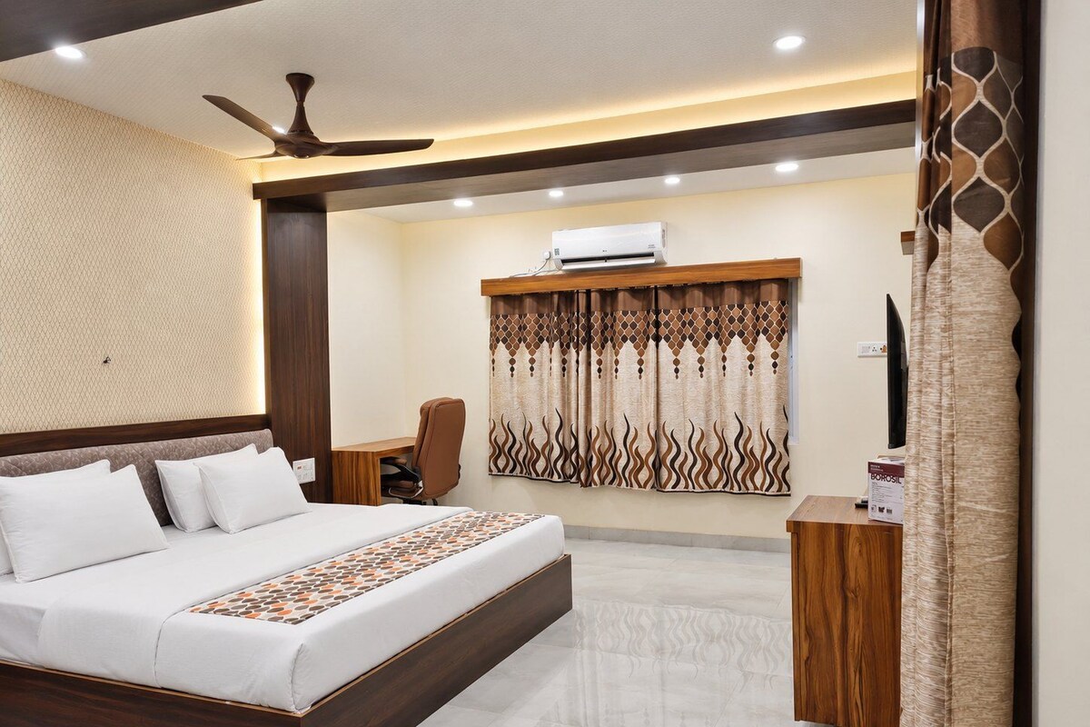A hotel room with a bed, desk, chair, air conditioning unit, and curtains.