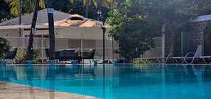 A swimming pool with lounge chairs and a covered seating area. - RK Resorts (Karaikal)