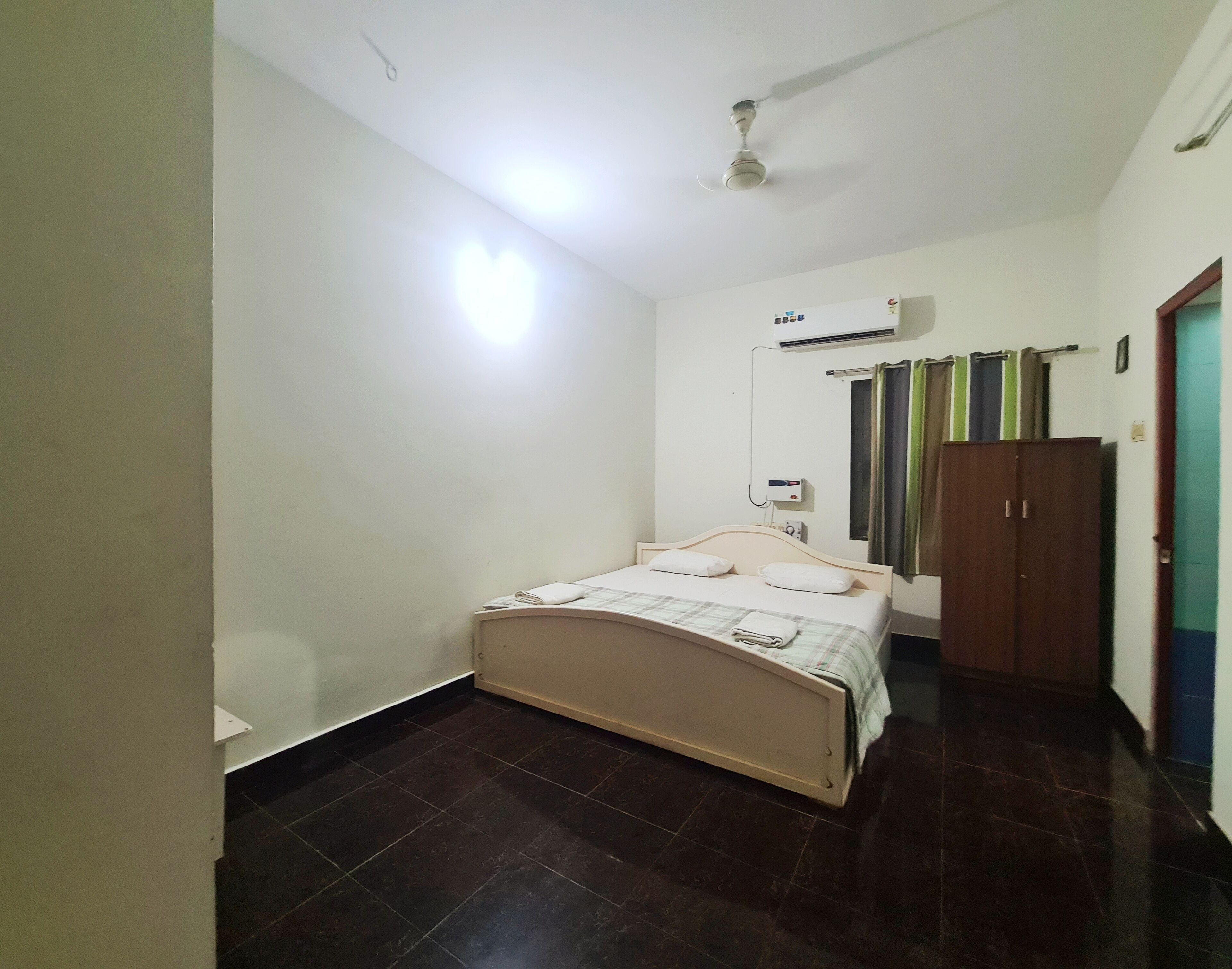 Une chambre à coucher comprenant un lit, un appareil de climatisation, un ventilateur de plafond et une armoire.