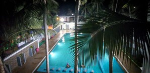 An indoor swimming pool with a clear view of the pool area, surrounded by palm trees and a covered seating area.