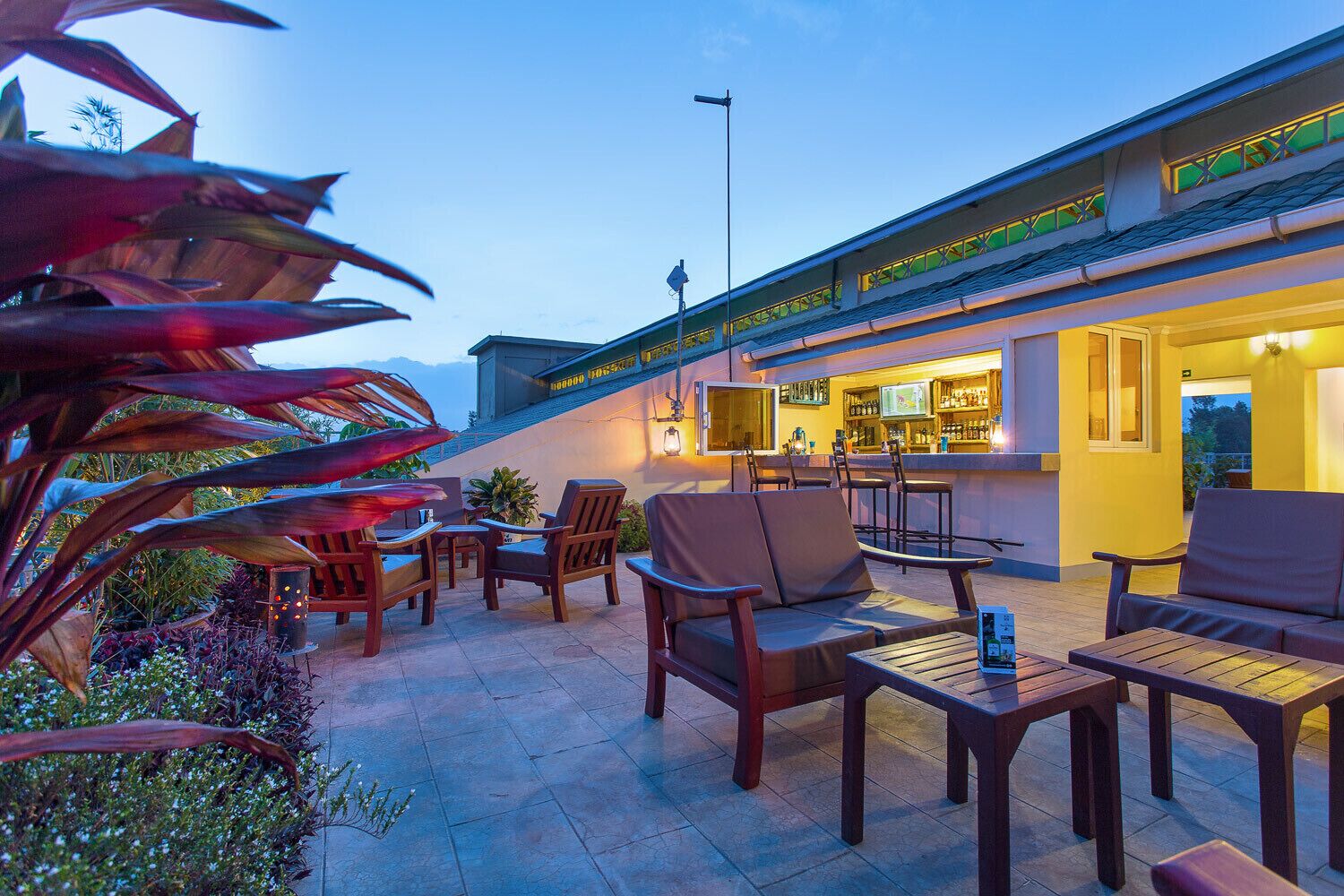 An outdoor bar area with wooden furniture, a bar counter, and a view of the mountains in the background.
