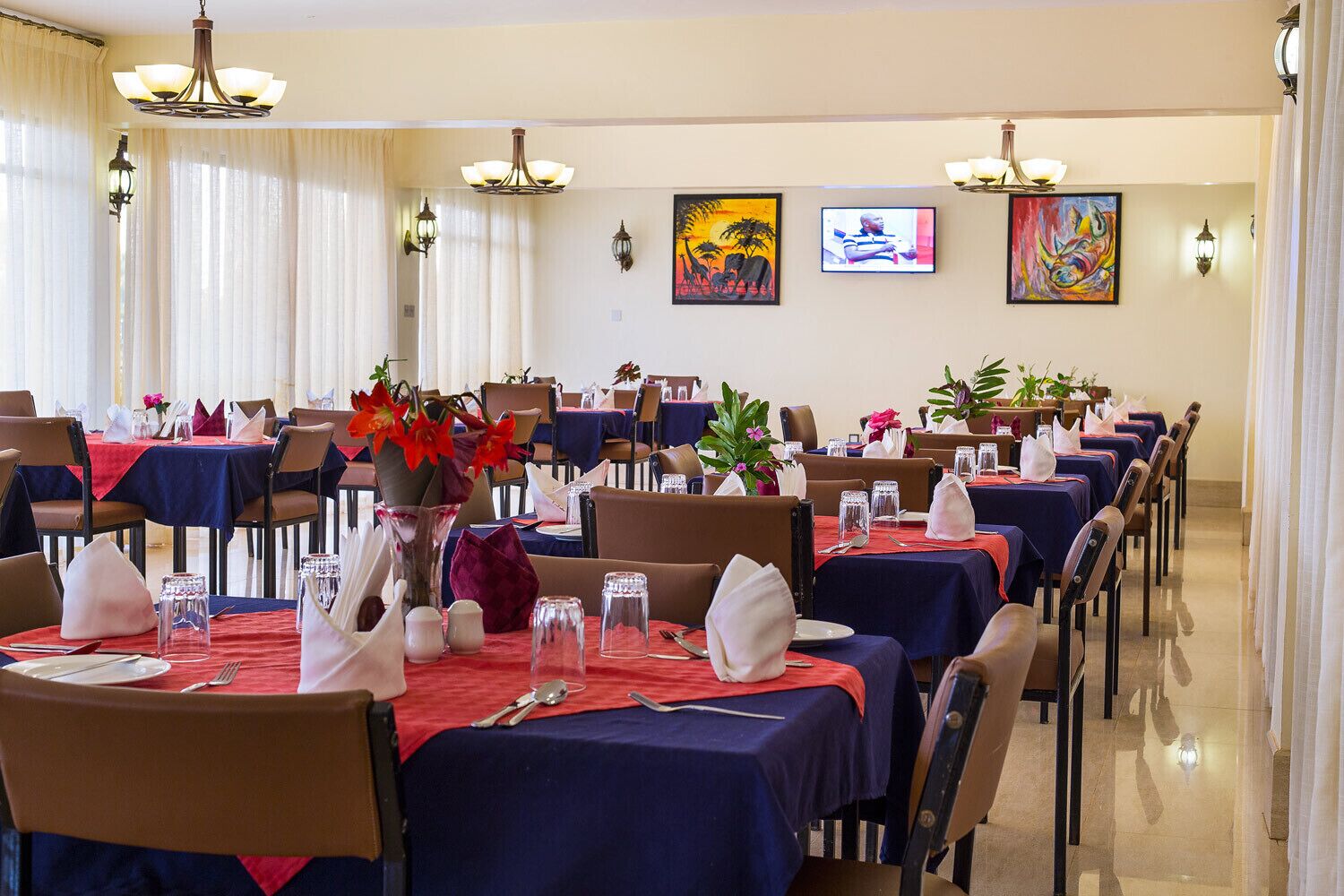 A dining area with tables set for service, featuring red tablecloths, white napkins, and floral centerpieces.