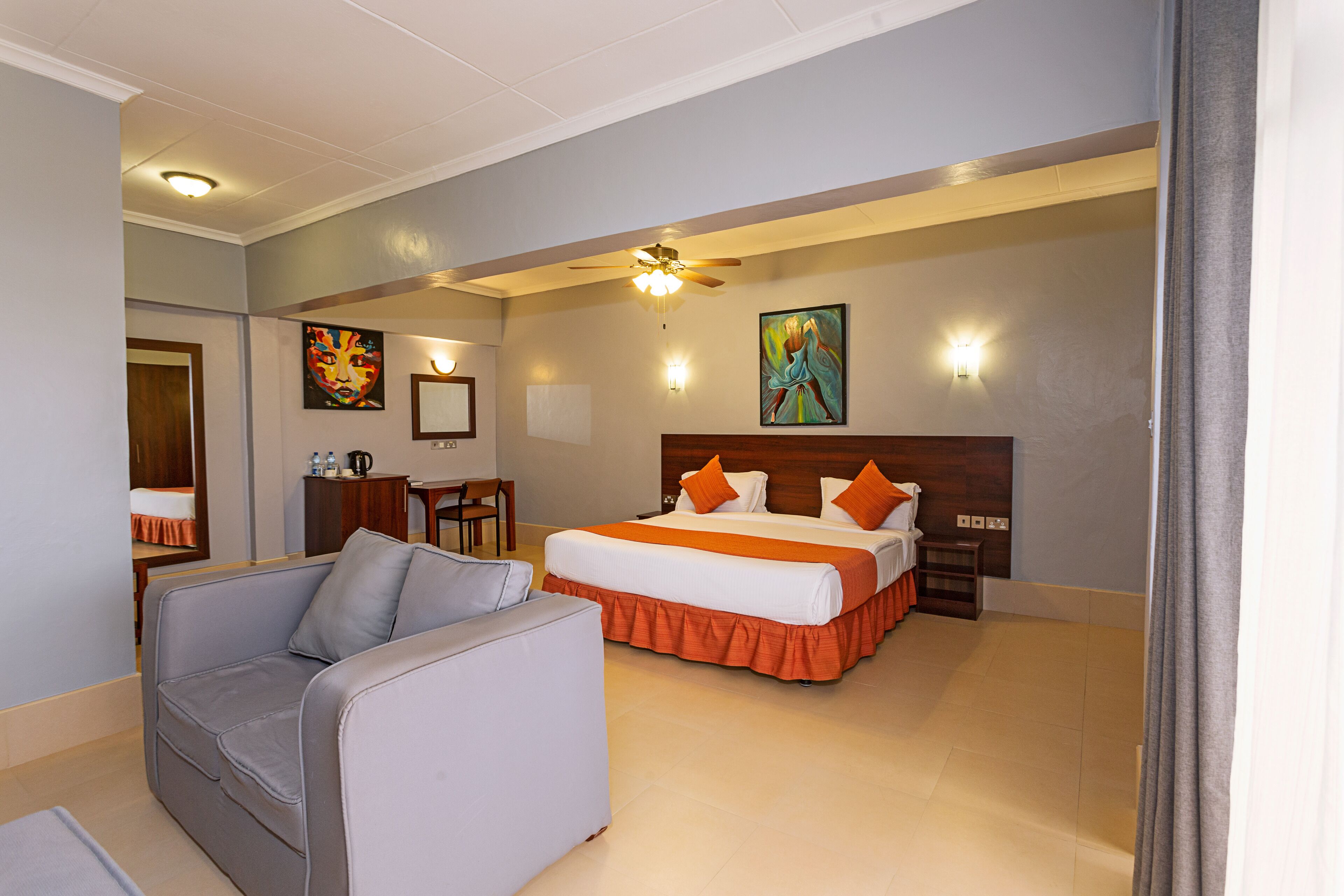 A hotel room with a bed, a sofa, a desk, and a ceiling fan.