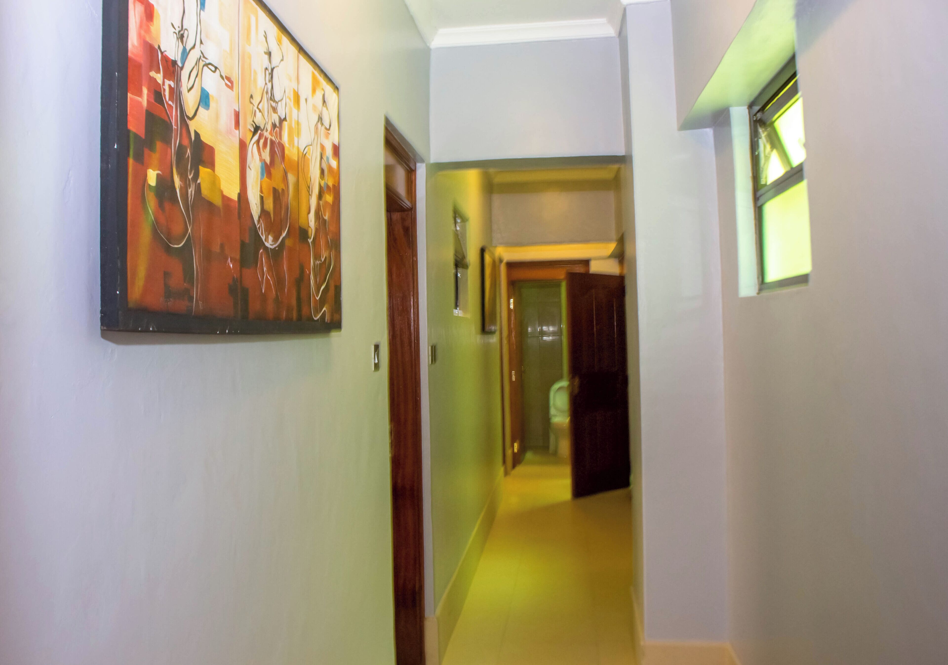 A hallway with a painting on the left, a door in the center, and a window on the right.
