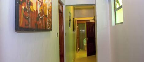 A hallway with a painting on the left, a door in the center, and a window on the right.