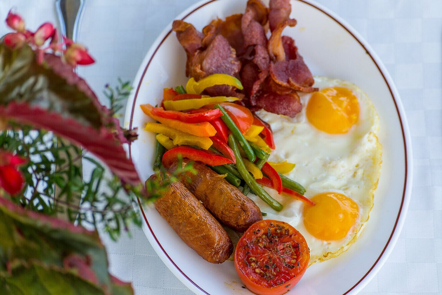A plate with eggs, bacon, sausages, peppers, and a tomato slice.