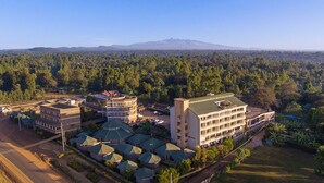An aerial view of a hotel complex with multiple buildings, surrounded by dense forest and a mountain in the background. - Roswam Hotel (Kerugoya)