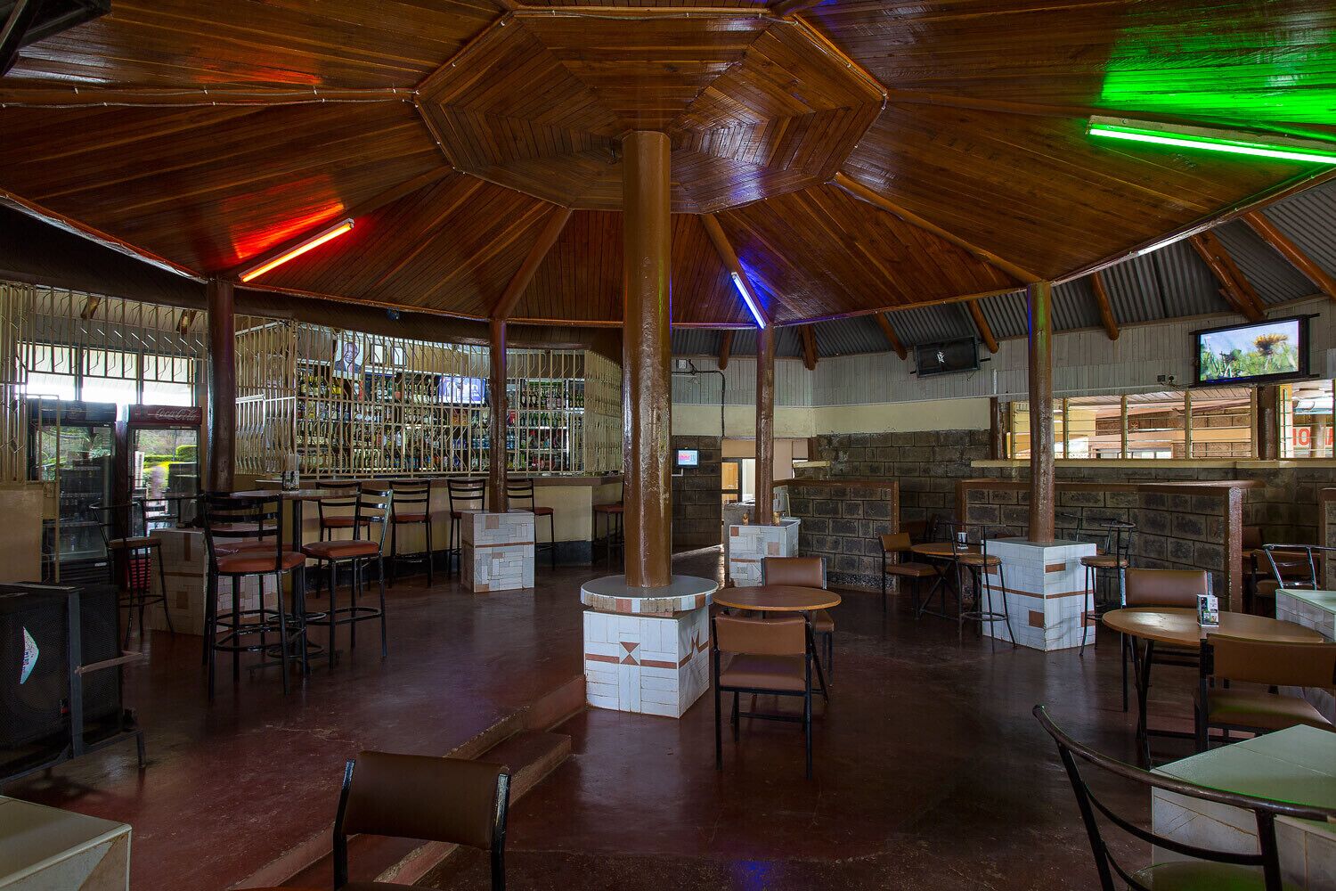 A spacious indoor area with multiple seating arrangements, a bar area with shelves of bottles, and a television screen mounted on the wall.