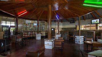 A spacious indoor area with multiple seating arrangements, a bar area with shelves of bottles, and a television screen mounted on the wall.