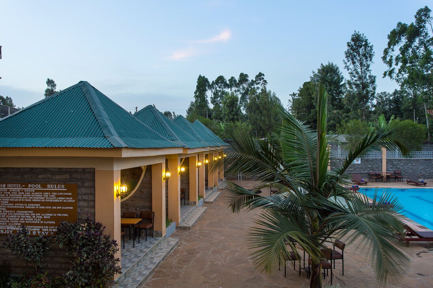 A hotel with a pool area, including a sign with pool rules and a view of the pool with lounge chairs.