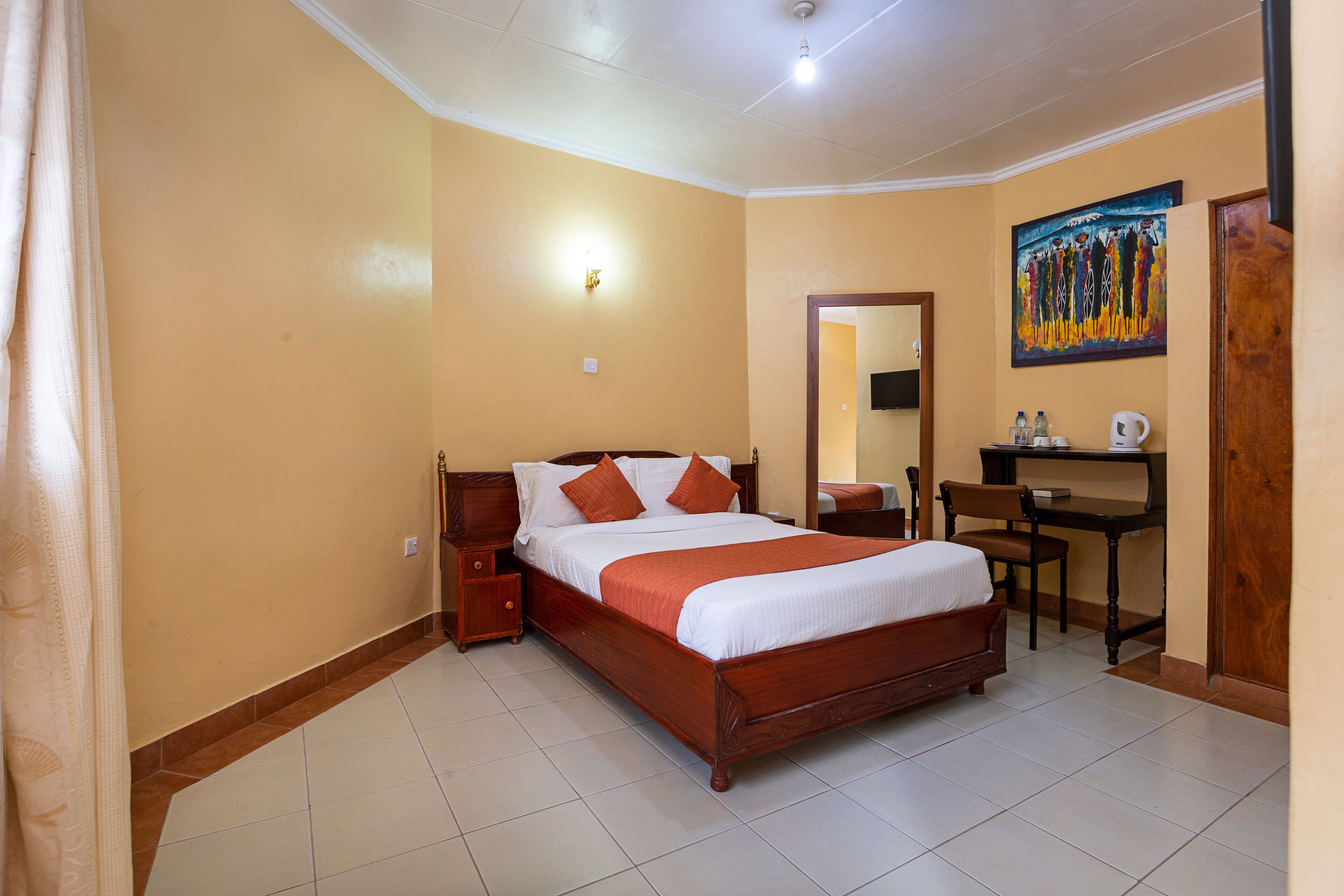 A bedroom with a wooden bed, a desk, a chair, and a painting on the wall.