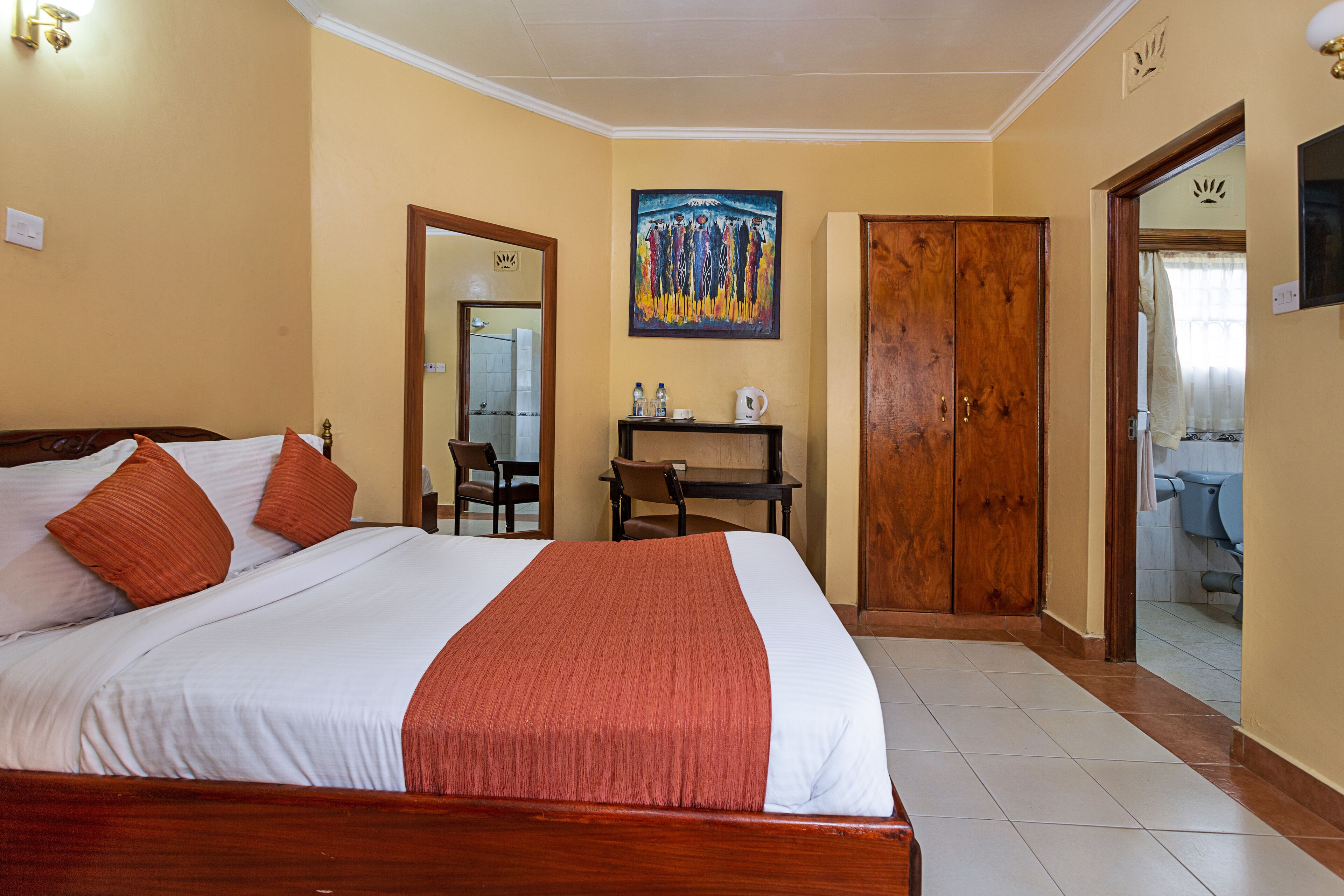Habitación de hotel con cama, escritorio, silla, un cuadro y baño visible a través de una puerta abierta.