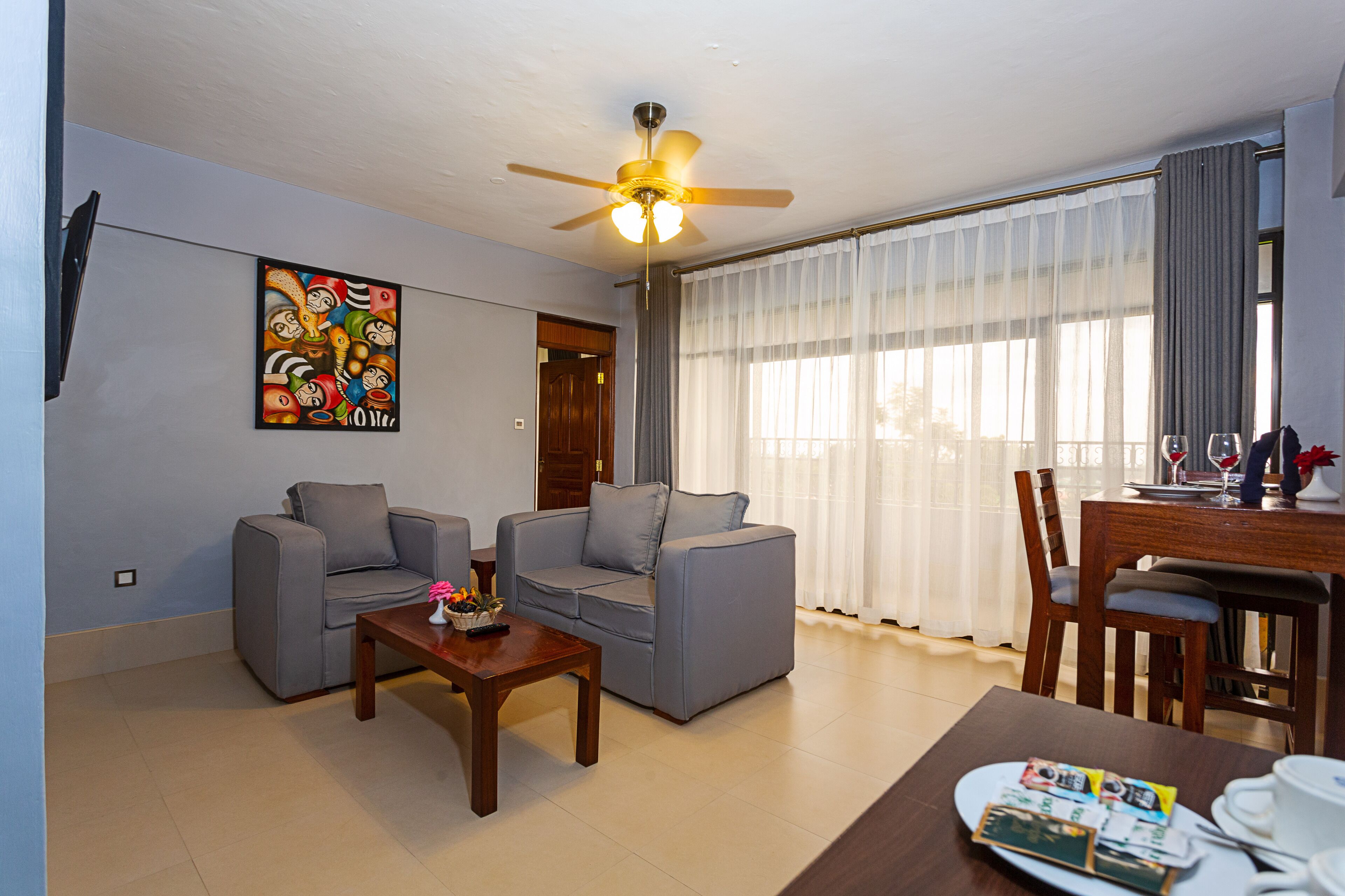 A living room with two grey sofas, a wooden coffee table, a ceiling fan, and a dining table with chairs.