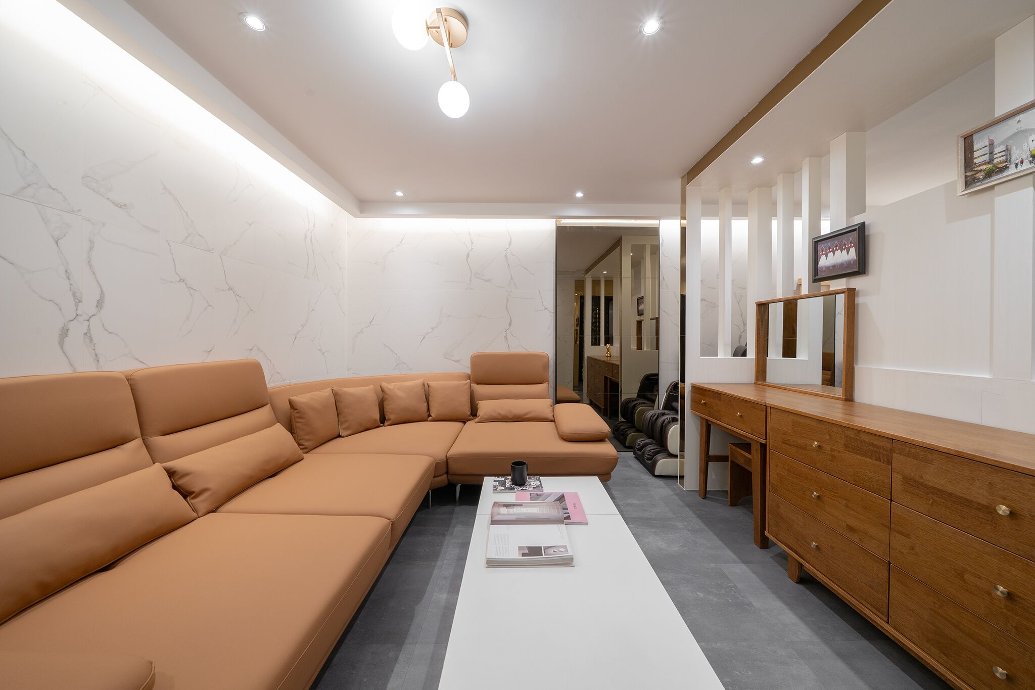 A modern living room with a sectional sofa, a coffee table with magazines, a wooden dresser, and a large mirror.