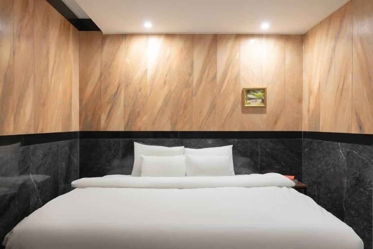 A modern hotel room with a large bed, marble walls, and a small painting on the wall.