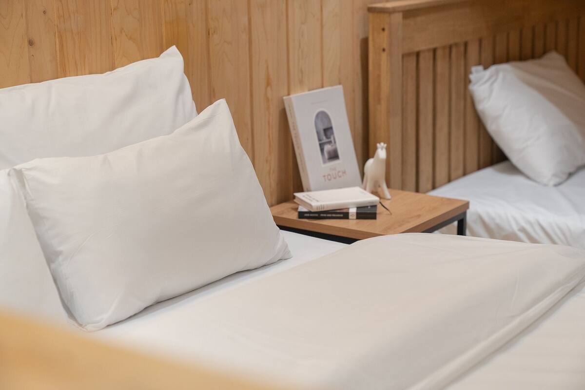 A hotel room with two beds, each with white bedding and pillows. There is a wooden headboard, a nightstand with a book and a small figurine.