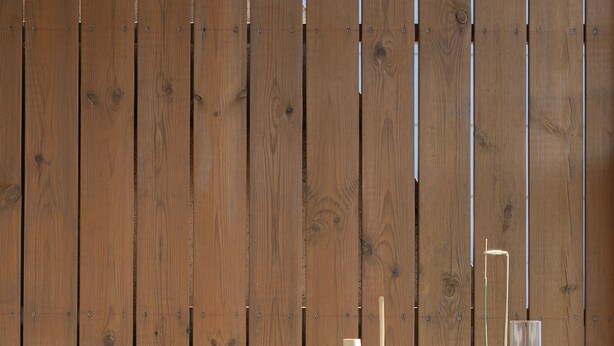 Une table en bois, sur laquelle se trouvent un bol blanc, une bouteille et un récipient en verre, le tout adossé à un mur en bois.