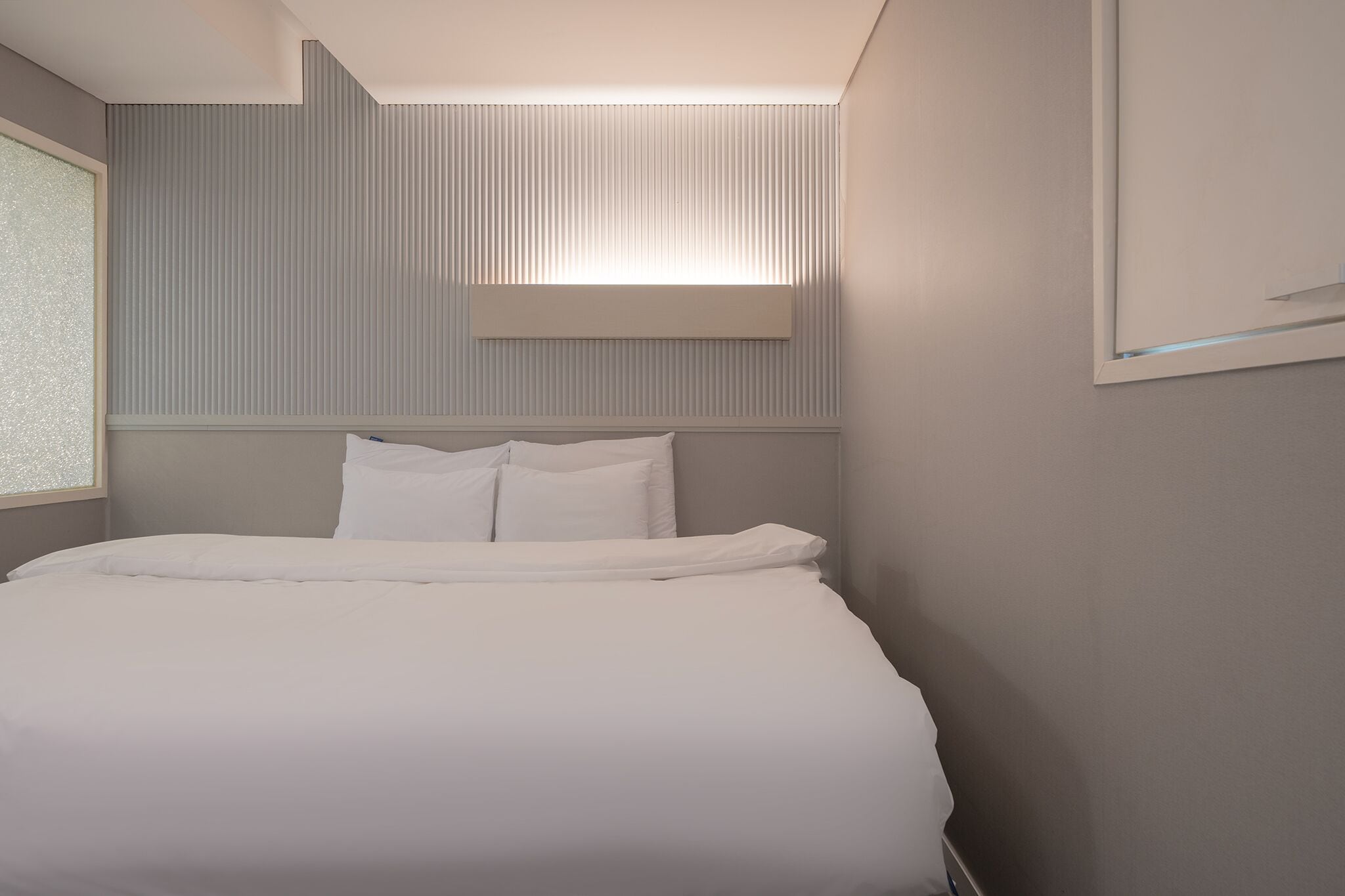 A modern hotel room with a neatly made bed, a large window, and a slanted ceiling design.