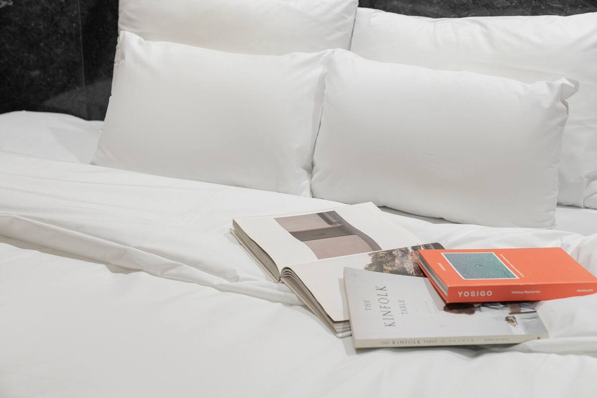 A neatly made bed with white linens, a book titled 'Holiday Memories', and another book with a visible title 'The Kinfolk'.