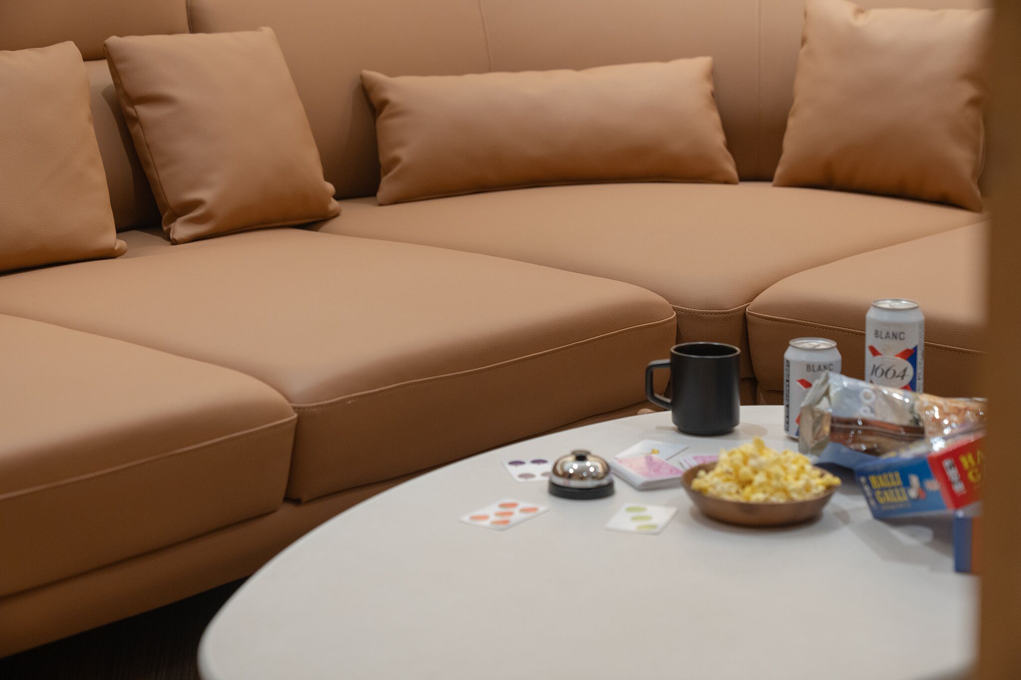 A beige sectional sofa with cushions, a white table with snacks, a can of beer, and a bottle of water.