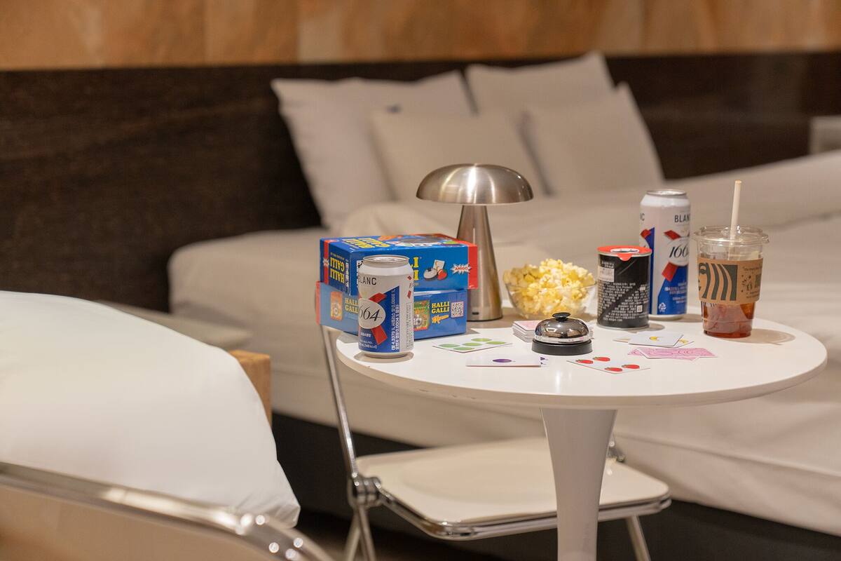 A neatly arranged hotel room with a bed, a bedside table with snacks, a lamp, and a chair.