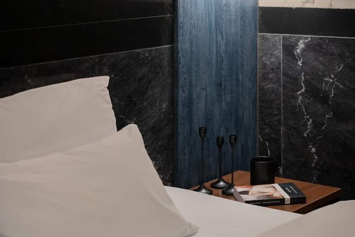 A bedroom with a bed, a bedside table with a book, a black mug, and a lamp.