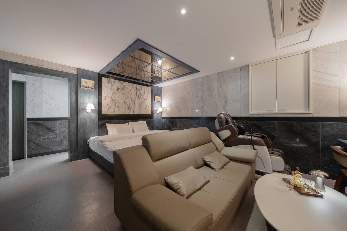 A modern hotel room with a large bed, a sofa, a dining table, and a skylight.