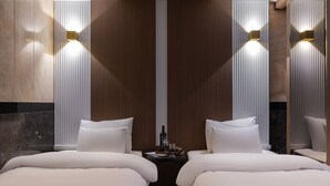 Une chambre d’hôtel avec deux lits, une petite table sur laquelle se trouvent une bouteille et des verres, et des lampes fixées au mur.