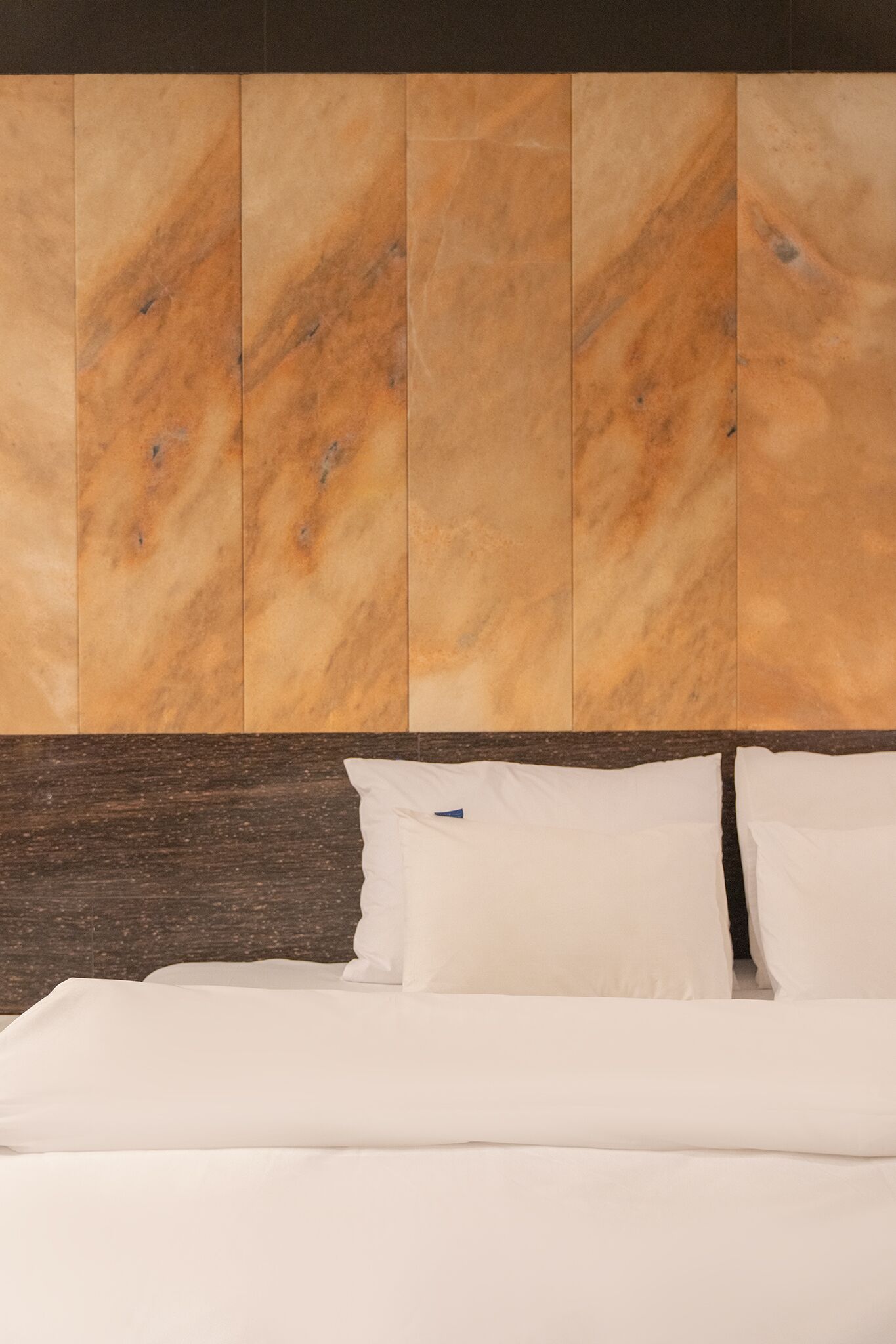 A hotel room with a marble headboard, white bedding, and a dark wooden headboard.