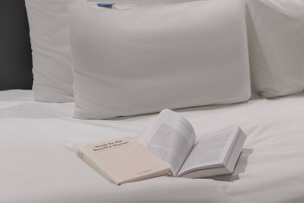 A neatly made bed with white linens and pillows, a book titled "Words for the Beautiful World" on it, and a wooden headboard.