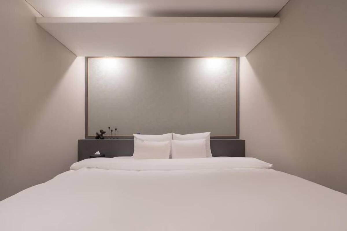 A modern hotel room with a large bed, a bedside table, and a wall-mounted mirror.