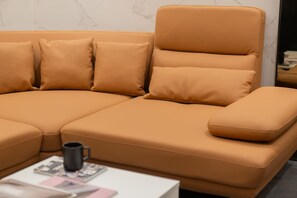 Un canapé moderne en cuir orange, agrémenté de plusieurs coussins, une tasse noire et un magazine posés sur une table blanche.