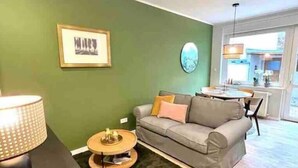 A living room with a green wall, a grey sofa, a round coffee table, and a lamp. - Im Herzen der Stadt - EG Wohnung (Paderborn)