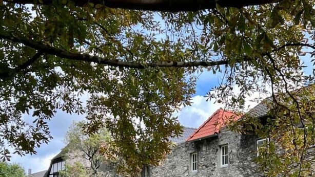 A stone building with multiple windows and a red roof, surrounded by a grassy area and trees. - Premium Apartment an der Stadtmauer im OG (Paderborn)