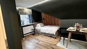 Un dormitorio compacto con cama, mesita de noche y una pequeña zona de comedor con mesa y sillas.