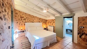 A bedroom with a stone wall, a bed with a white headboard, a radiator, and a door leading to a bathroom. - Cream Homes Son Celles Etv3533, Casa de Campo Recién Reformada (Sancellas)