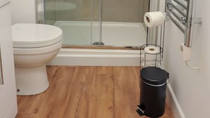 A bathroom with a glass-enclosed shower, a toilet, a black trash bin, and a towel rack.