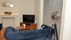 A living room with a blue sofa, a wooden coffee table, a flat-screen TV, and a decorative mirror on the wall.
