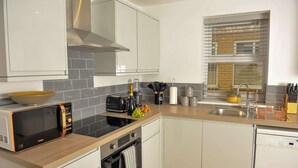 Une cuisine moderne avec des meubles blancs, une cuisinière noire, un four à micro-ondes et une fenêtre avec des stores.