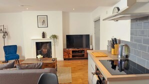 A modern living room with a fireplace, a television, and a kitchen area with a stove. - 50 Queens Road Apartment 3 (Reading)