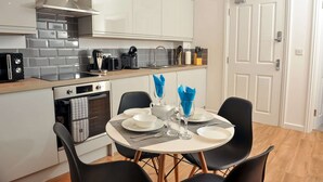 A modern kitchen with white cabinets, a built-in oven, and a dining area with a round table and black chairs. - 50 Queens Road Apartment 3 (Reading)