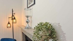 A living room with a fireplace, a blue sofa, a floor lamp, and a potted plant. - 50 Queens Road Apartment 3 (Reading)