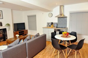 Een moderne woonkamer met een bank, televisie, open haard en een eetgedeelte met stoelen en een tafel.