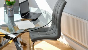 A modern office space with a glass desk, a laptop, a black leather chair, and a vase with flowers. - The Pavilion by Select SA (Windsor)